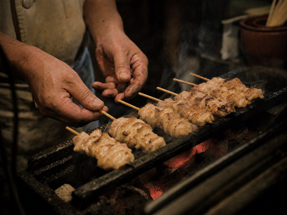 炭火の上で串を返す焼き手の手元と、立ちのぼる煙